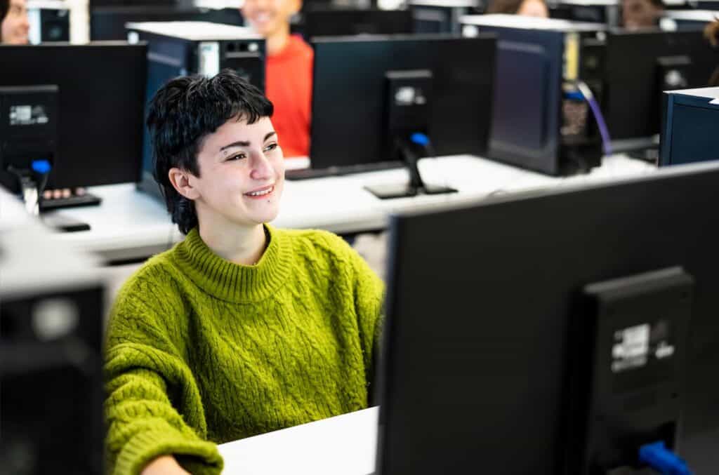 A student smiles as they work at a computer in a lab.