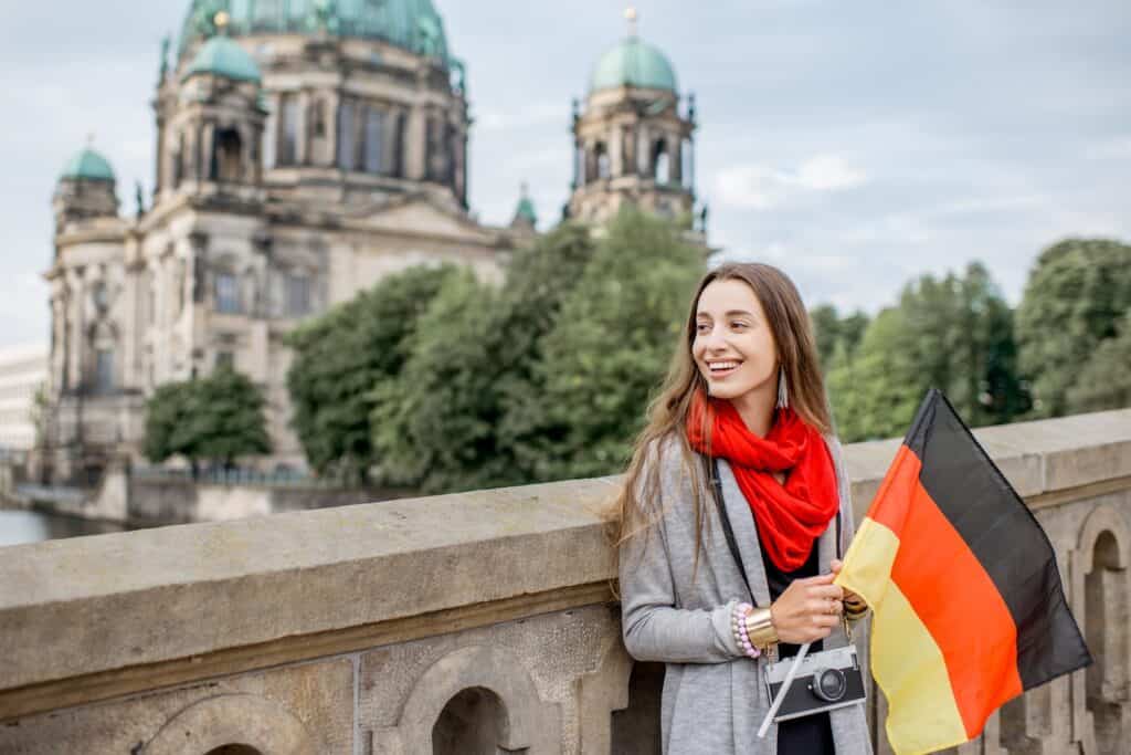 A woman smiles as she poses with a German flag while standing in a historic area in Berlin.