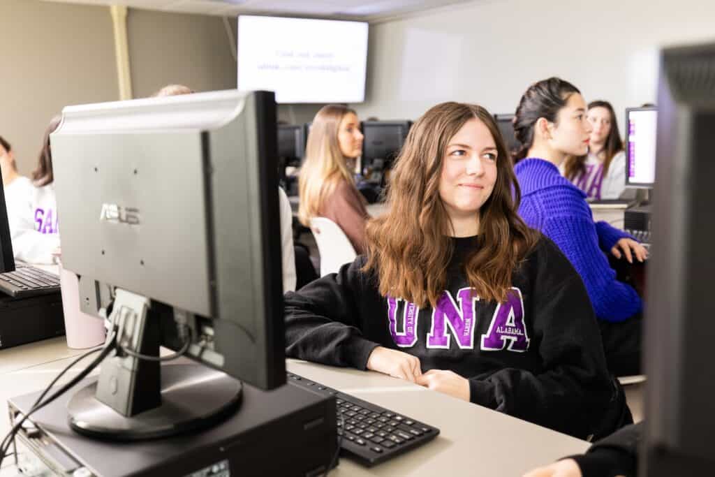 A University of North Alabama student smiles as she sits in a a computer lab with fellow students.